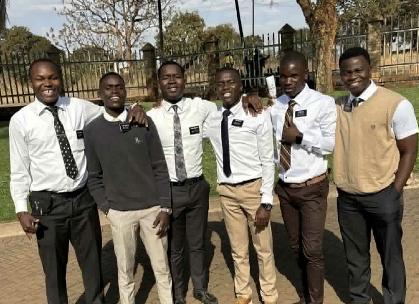 Six young returned missionaries in shirts and ties standing together outdoors, smiling